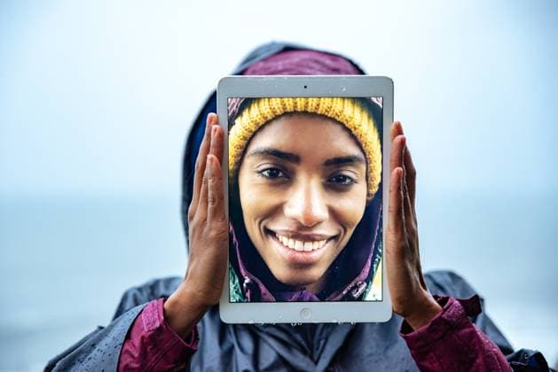 Creative Highlights Symbolbilder Portrait of cheerful young female traveler in raincoat covering face with digital tablet with self photo on screen against sea under blue sky, Model released DavidPrado_ID12972_394679_037 Copyright: xDavidxPradox MR