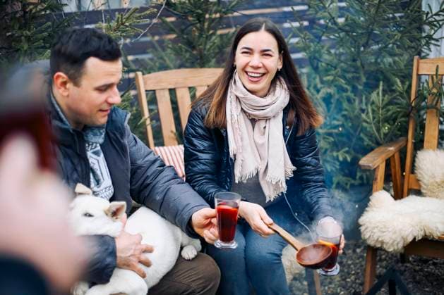 Winter bonfire party. Joyful young couple with dog drinking hot mulled wine in company of friends Bonfire party. Joyful young family couple gathering with friends around campfire in winter, happy people preparing and drinking hot mulled wine while enjoying picnic on backyard in wintertime Copyright: xZoonar.com DashaxPetrenkox 18978434 ,model released, Symbolfoto ,property released