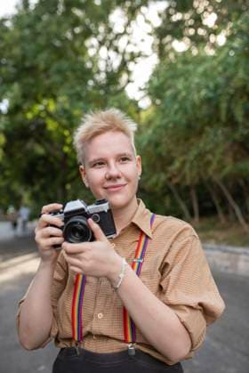 Smiling non-binary person with camera standing in park model released, Symbolfoto, VRAF00015