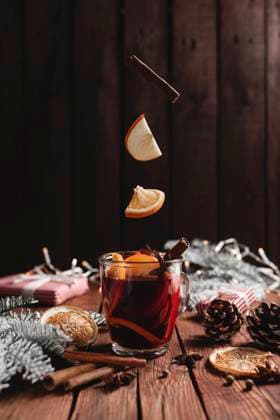 Christmas cup of Mulled Wine on table, levitating cinnamon stick, orange, apple Christmas glass cup or mug with Mulled Wine on wooden table and background with levitating cinnamon stick, dried or sublimated orange, apple slices, present gift boxes, garlands, decoration lights Copyright: xZoonar.com OlenaxIvanovax 17654126