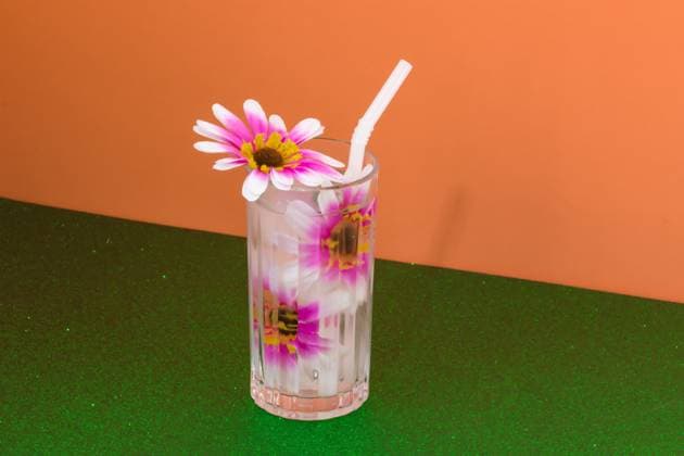 Transparent glass of refreshing cold drink decorated with pink flowers and straw placed on green surface against bright orange wall Rodobot_ID12962_394298_002 Copyright: xRodobotx Model Released