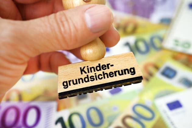 FOTOMONTAGE, Hand hÃ¤lt Stempel mit Schriftzug Kindergrundsicherung Ã¼ber Geldscheinen *** PHOTOMONTAGE, hand holding stamp with writing child basic security over banknotes ** NUR FUER REDAKTIONELLE ZWECKE ** EDITORIAL USE ONLY **