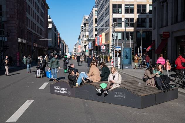 28.02.2023, Berlin, Deutschland, Europa - Fussgaenger gehen im Berliner Bezirk Mitte ueber die autofreie Friedrichstrasse, vorbei an sitzenden Menschen auf Stadtmoebeln. Der Teilabschnitt zwischen Franzoesischer Strasse und Leipziger Strasse ist seit kurzem dauerhaft autofrei und nicht mehr befahrbar. *** 28 02 2023, Berlin, Germany, Europe Pedestrians walk along the car-free Friedrichstrasse in Berlins Mitte district, passing people sitting on city furniture The section between Franzoesischer Strasse and Leipziger Strasse has recently been made permanently car-free and no longer accessible to traffic