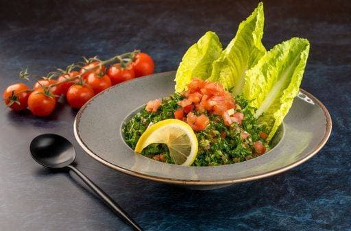 RECORD DATE NOT STATED A closeup shot of a gray plate of Taboula salad with tomatoes and a spoon on the table *** einer closeupe erschossen des einer graüm Teller des Taboula Salat mit Tomaten und einer löffeln am der Tisch 13007398