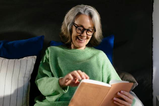 Smiling mature woman reading book in bedroom model released, Symbolfoto property released, EBSF02835