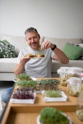 Happy mature man putting bean sprouts on toasted bread in living room at home model released, Symbolfoto property released, HMEF01554