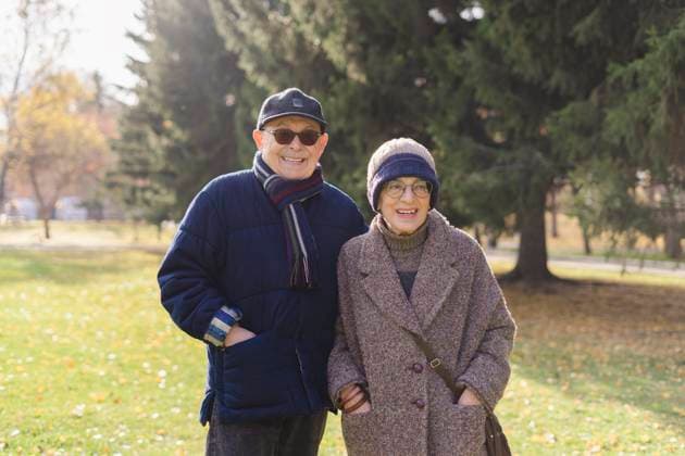 Smiling senior couple with hands in pockets standing at park model released, Symbolfoto, SEAF01781