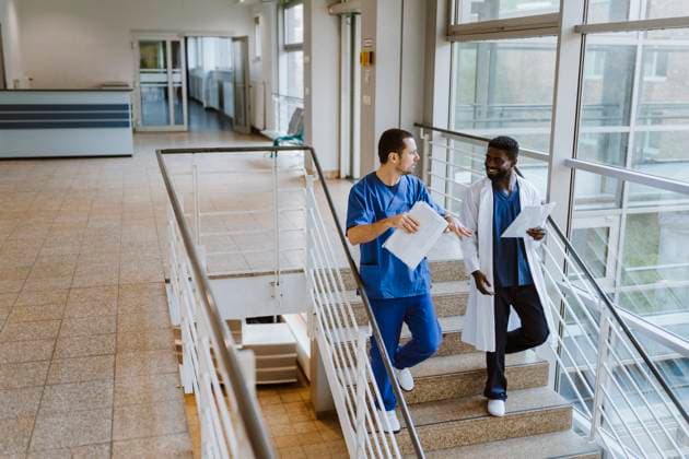 Full length of male doctor and nurse discussing over documents while moving down on staircase in hospital Germany, Berlin, model released, property released Copyright: xMaskotx , MA100131 MA100131