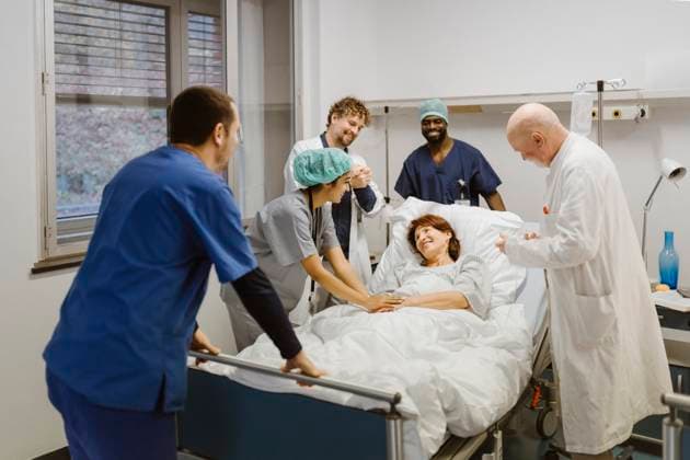 Smiling healthcare workers cheering while standing around senior female patient at hospital Germany, Berlin, model released, property released Copyright: xMaskotx , MA100161 MA100161