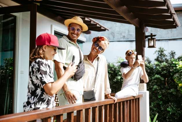 Smiling parents looking at daughter using smart phone standing by son on porch of villa Thailand, Ko Lanta, model released, property released Copyright: xMaskotx , MA100476 MA100476