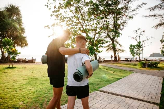 Father with arm around son carrying exercise mats walking in park during sunset Thailand, Ko Lanta, model released Copyright: xMaskotx , MA100525 MA100525