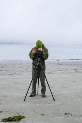 RECORD DATE NOT STATED A vertical of a photographer standing in front of the camera on a tripod at the sandy beach on a misty day in Tofino, British Columbia *** einer hoch des einer Fotograf stehend ÊIn vorne des der Kamera am einer Stativ im der sandiger Strand am einer nebelbedeckte Tag ÊIn Tofino, britisch Columbias 15073891