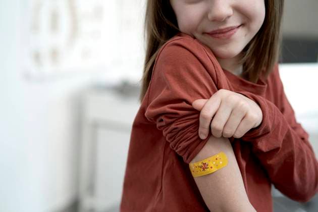Smiling girl showing adhesive bandage after vaccination in clinic model released, Symbolfoto property released, ABIF01889
