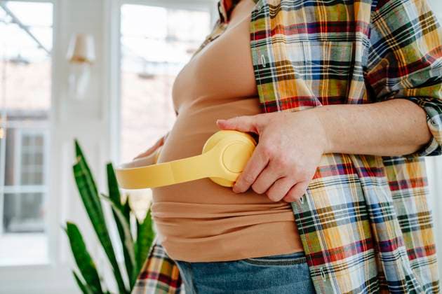 Pregnant woman holding headphones on belly at home model released, Symbolfoto property released, MDOF01039
