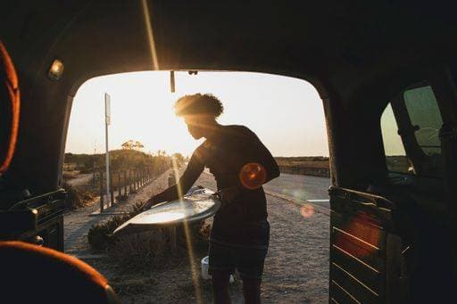 A young, black surfer with curly hair catching a surfboard in caravan at sunset *** einer young, Schwarz Surferin mit Korkenzieherlocken Haare fangende einer Surfbrett ÊIn Wohnwagen im Sonnenuntergang 2686575 ,model released, Symbolfoto
