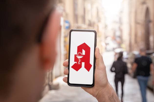 Augsburg, Bavaria, Germany - 26 April 2023: Man holding on smartphone app with a German pharmacy logo. Symmbol image Digital Medicine PHOTOMONTAGE *** Mann hält auf Smartphone App mit einem deutschen Apotheke Logo. Symmbolbild Digitale Medizin FOTOMONTAGE