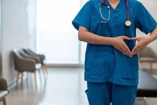 A shallow focus of a doctor in scrubs making heart hand gesture at a hospital hallway *** einer seicht Fokus des einer Arzt ÊIn scheuert machend Herz handgeschnitzten Geste im einer Krankenhaus Hausgang 2870492