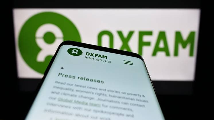 Mobile phone with webpage of confederation Oxfam International on screen in front of logo. Stuttgart, Germany - 01-21-2023: Mobile phone with webpage of confederation Oxfam International on screen in front of logo. Focus on top-left of phone display. Copyright: xZoonar.com TimonxSchneiderx 19761307