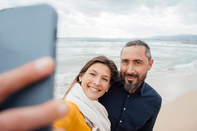 Happy woman taking selfie with mature man through mobile phone at beach model released, Symbolfoto, JOSEF18492
