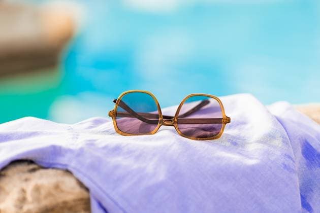 Close up of fashionable hexagonal purple sunglasses with folded arms placed on a white towel on a stone against blue water faded in the sunlight HodeiUnzueta_ID14021_423068_033 Copyright: xHodeixUnzuetax Model Released
