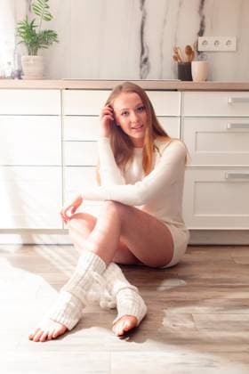 Young woman sitting on the floor in the kitchen Attractive young woman sitting on the wooden floor at home, touching her loose blond hair. An adorable model posing in white short warm dress and knitted stockings in modern white kitchen. ,model released, Symbolfoto Copyright: xZoonar.com OksanaxShufrychx 15108250 ,model released, Symbolfoto ,property released