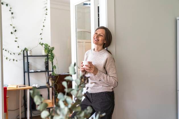 IMAGO Creative: Frühjahrsputz Happy mature woman leaning on wall with coffee cup model released, Symbolfoto property released, VPIF08088
