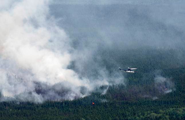 July 5, 2023, Lebel-sur-Quevillon, PQ, Canada: A helicopter carrying a water basket flies past a smoke plume near Lebel-sur-Quevillon, Que., Wednesday, July 5, 2023. Lebel-sur-Quevillon Canada  - ZUMAc35_ 20230705_zaf_c35_067 Copyright: xAdrianxWyldx