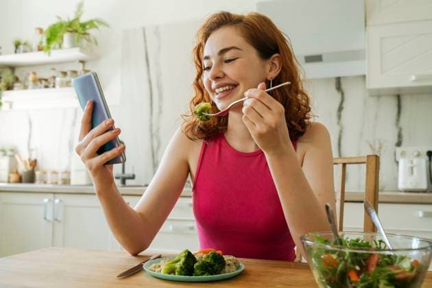 Happy young woman using smart phone and having salad at dining table model released, Symbolfoto property released, OSF01772