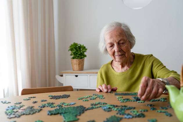 Elderly woman solving jigsaw puzzle on table model released, Symbolfoto property released, SVKF01488