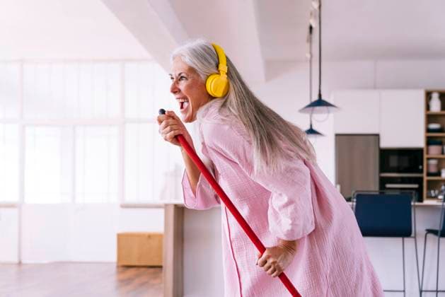 Carefree woman with yellow headphones listening to music holding broom at home model released, Symbolfoto property released, OIPF03356