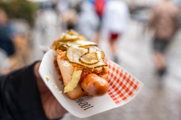 Copenhagen, Denmark - 17 July 2023: Hand holding an original Danish hotdog. Hotdog with sausage, bread, pickles and fried onions in the city *** Hand hält einen original dänischen Hotdog. Hotdog mit Wurst, Brot, Gurken und Röstzwiebeln in der Stadt