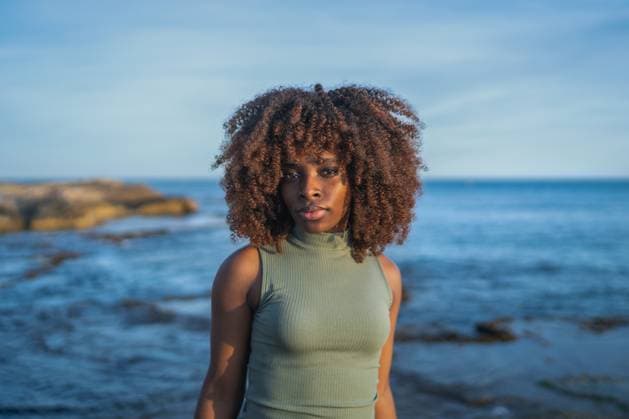 Serious African american young woman in dress looking at camera while standing against blurred beach in daylight Model Released OscarDeDios_ID16049_488502_002 Copyright: xOscarxDexDiosx