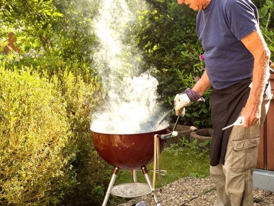 An elderly gentleman lights the charcoal and produces a lot of smoke in Biessenhofen, Bavaria, Germany, July 22, 2023. Model Released