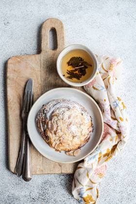 Top view of sweet almond pastry on wooden chopstick between fork and knife and napkin with cup of green tea against gray background Model Released AnnaBogush_ID16101_490205_002 Copyright: xAnnaxBogushx