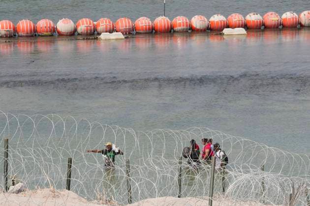 USA, Migranten aus Mittelamerika am Rio Grande in Eagle Pass, Texas August 21, 2023, Eagle Pass, TX, United States: A group of migrants look for an opening in the concertina wire barrier south of Eagle Pass where a 1000-foot string of buoys has been placed in the river to deter crossing the Rio Grande River into Texas. The migrants later found an opening and crossed into the United States as several U.S. governors were touring overhead by helicopter. Eagle Pass United States - ZUMAd150 20230821_znp_d150_042 Copyright: xBobxDaemmrichx