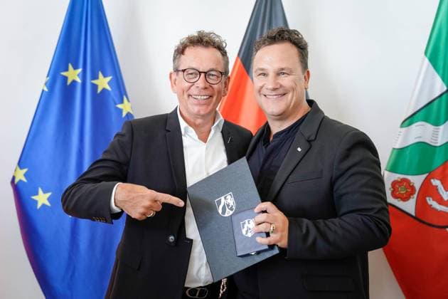 Verleihung des Verdienstorden des Landes Nordrhein-Westfalen Guido Maria Kretschmer aus Hamburg der Modedesigner und beliebte Moderator mit seinem soeben ueberreichten Verdienstorden und seinem Ehemann Frank Mutters deutet auf den Verdienstorden seines Mannes im Anschluss an die Verleihung des Verdienstorden des Landes Nordrhein-Westfalen in der Staatskanzlei in Duesseldorf, Düsseldorf, 22.08.2023 Duesseldorf Nordrhein-Westfalen Deutschland *** Award of the Order of Merit of the State of North Rhine Westphalia Guido Maria Kretschmer from Hamburg the fashion designer and popular presenter with his just presented Order of Merit and his husband Frank Mutters points to the Order of Merit of his husband following the award of the Order of M