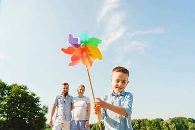 Smiling boy holding rainbow pinwheel with parents in background model released, Symbolfoto property released, IHF01514