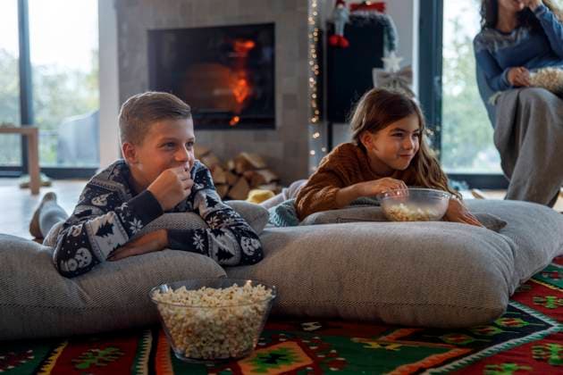 IMAGO Creative, Weihnachten, Tradition: Weihnachtsfilme sehen Smiling siblings watching TV with mother and eating popcorn at home model released, Symbolfoto property released, IKF01089