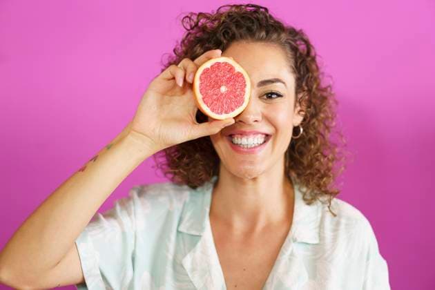 Happy woman holding grapefruit over eye against magenta background model released, Symbolfoto property released, JSMF02882