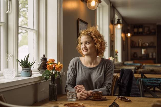 IMAGO Creative, Jahreszeit Frühling, Licht und Sonne Happy young woman sitting at table with coffee Hveragerði, Iceland CR_OSBJ230828-1242931-01 ,model released, Symbolfoto ,property released