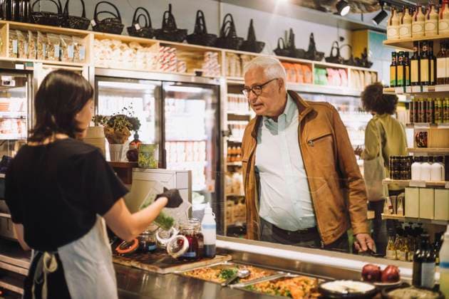 Saleswoman showing container to senior male customer at delicatessen Sweden, Stockholm, model released, property released Copyright: xMaskotx , MA102570 MA102570