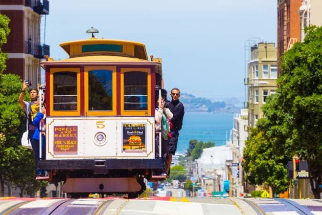 San Francisco Bay Coming Cable Car Front Close H San Francisco, USA - May 19, 2016: Approaching iconic cable car is full of outside hanging and platform standing tourists with bay water background in sunny Powell Street in California. Horizontal Copyright: xZoonar.com PiusxLeex 9896579