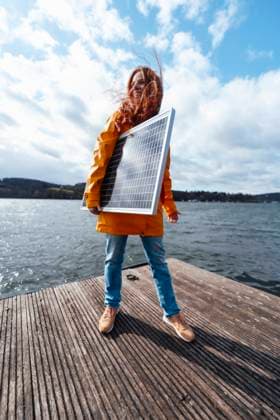 Woman with solar panel standing on pier under cloudy sky by lake model released, Symbolfoto, KNSF09772