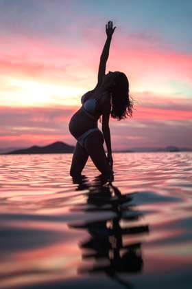 Creative Highlights Symbolbilder Pregnant woman stretching arm standing in sea water at sunset model released, Symbolfoto, DMHF00156