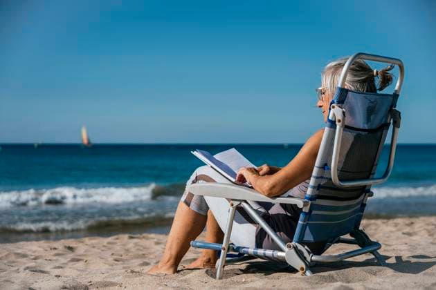 Mature woman sitting on deck chair and reading book at beach model released, Symbolfoto, GDBF00084