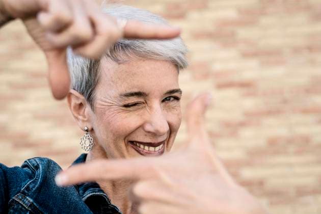 Creative Highlights Symbolbilder Smiling woman winking and showing finger frame sign in front of wall model released, Symbolfoto, JCZF01266
