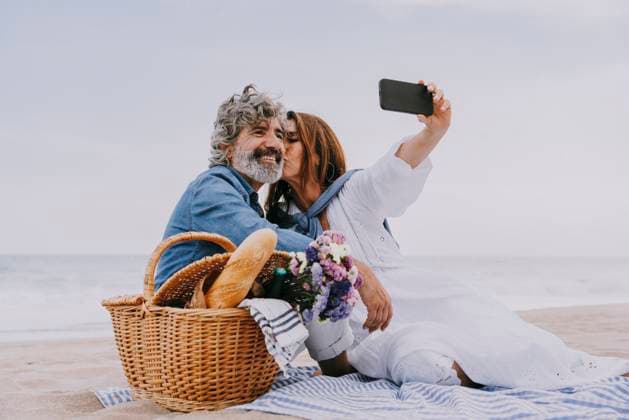 Creative Highlights Symbolbilder Happy senior woman kissing man and taking selfie through smart phone at beach model released, Symbolfoto, OIPF03512