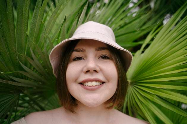 Smiling woman wearing bucket hat near palm leaves model released, Symbolfoto, YBF00169