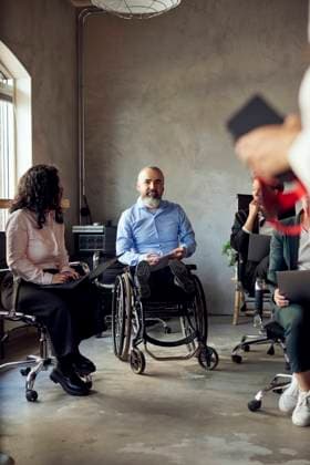 Businessman with disability sitting on wheelchair by female colleague during meeting in office Sweden, Gothenburg, model released, property released Copyright: xMaskotx , MA103899 MA103899