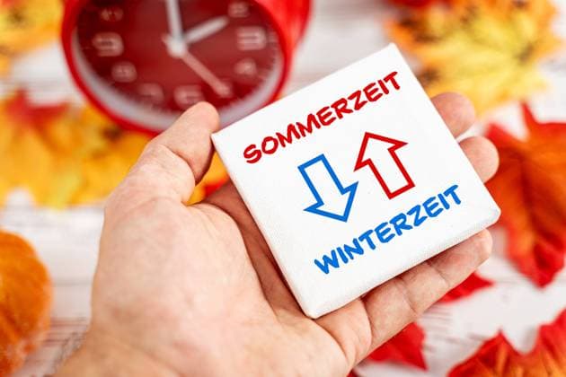 9 October 2023: Daylight saving time and winter time with two arrows on a board in one hand. Symbol image time change in autumn PHOTOMONTAGE *** Sommerzeit und Winterzeit mit zwei Pfeilen auf einer Tafel in einer Hand. Symbolbild Zeitumstellung im Herbst FOTOMONTAGE
